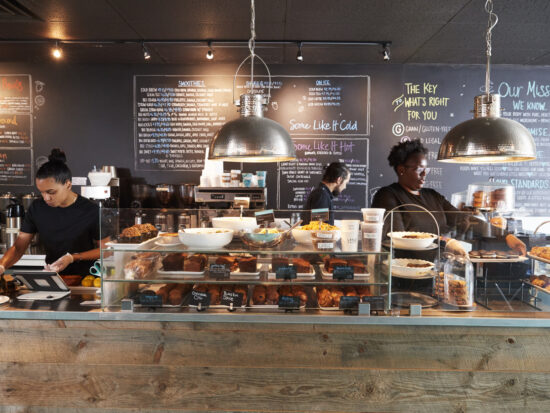 Baristas preparing drinks behind a rustic coffee shop counter with a display of pastries and chalkboard menus, showcasing a cozy, Instagrammable café atmosphere in Destin, Florida.