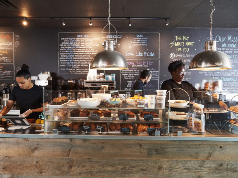 Baristas preparing drinks behind a rustic coffee shop counter with a display of pastries and chalkboard menus, showcasing a cozy, Instagrammable café atmosphere in Destin, Florida.
